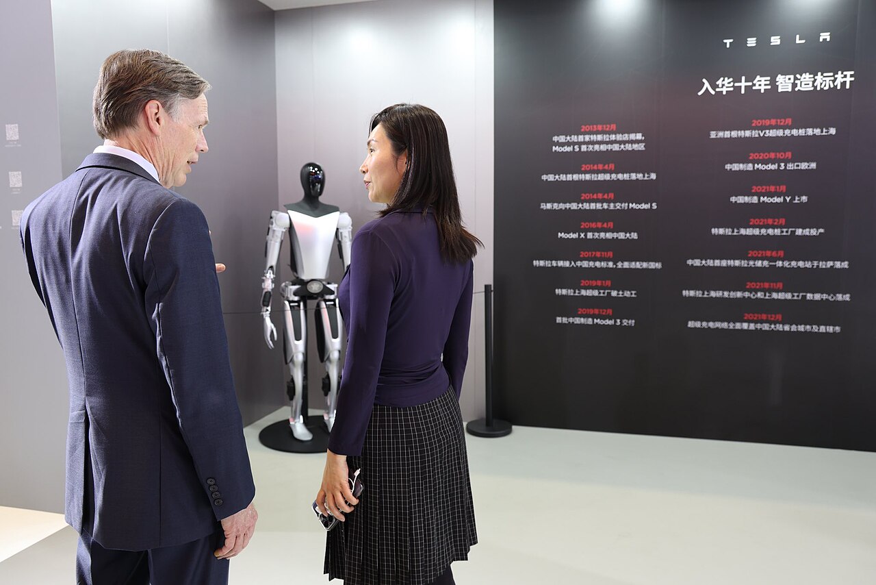 Visitors inspecting a Tesla Optimus humanoid robot display